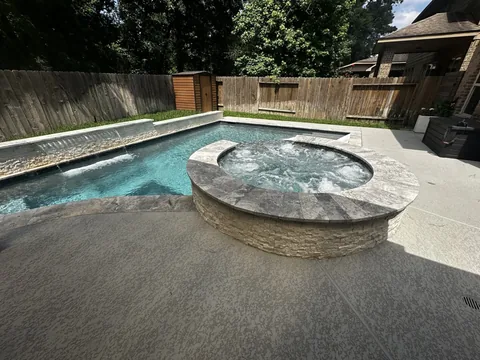 Raised circular spa beside a pool with a water feature wall