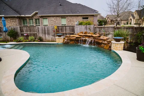Backyard pool with a rock waterfall and surrounding landscaping