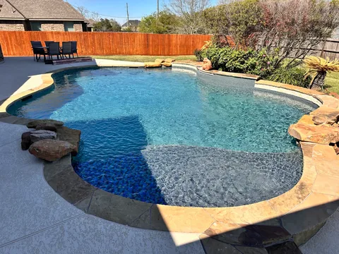 Curved backyard pool with stone edging and landscaping